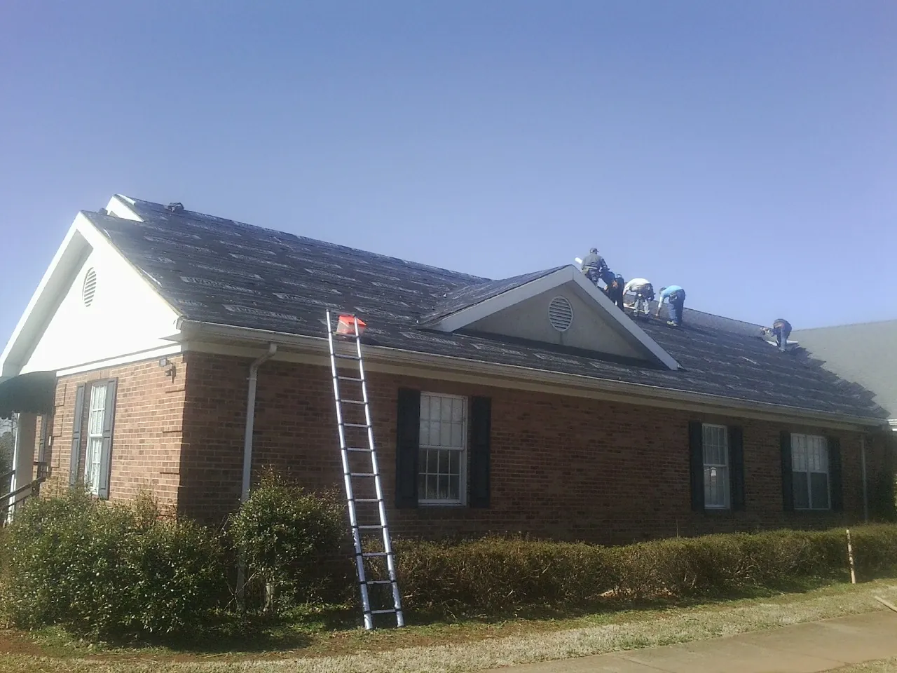 Crew tearing shingles off a brick ranch roof with a ladder set — Metal Roof Repair work by our crew in Beachwood