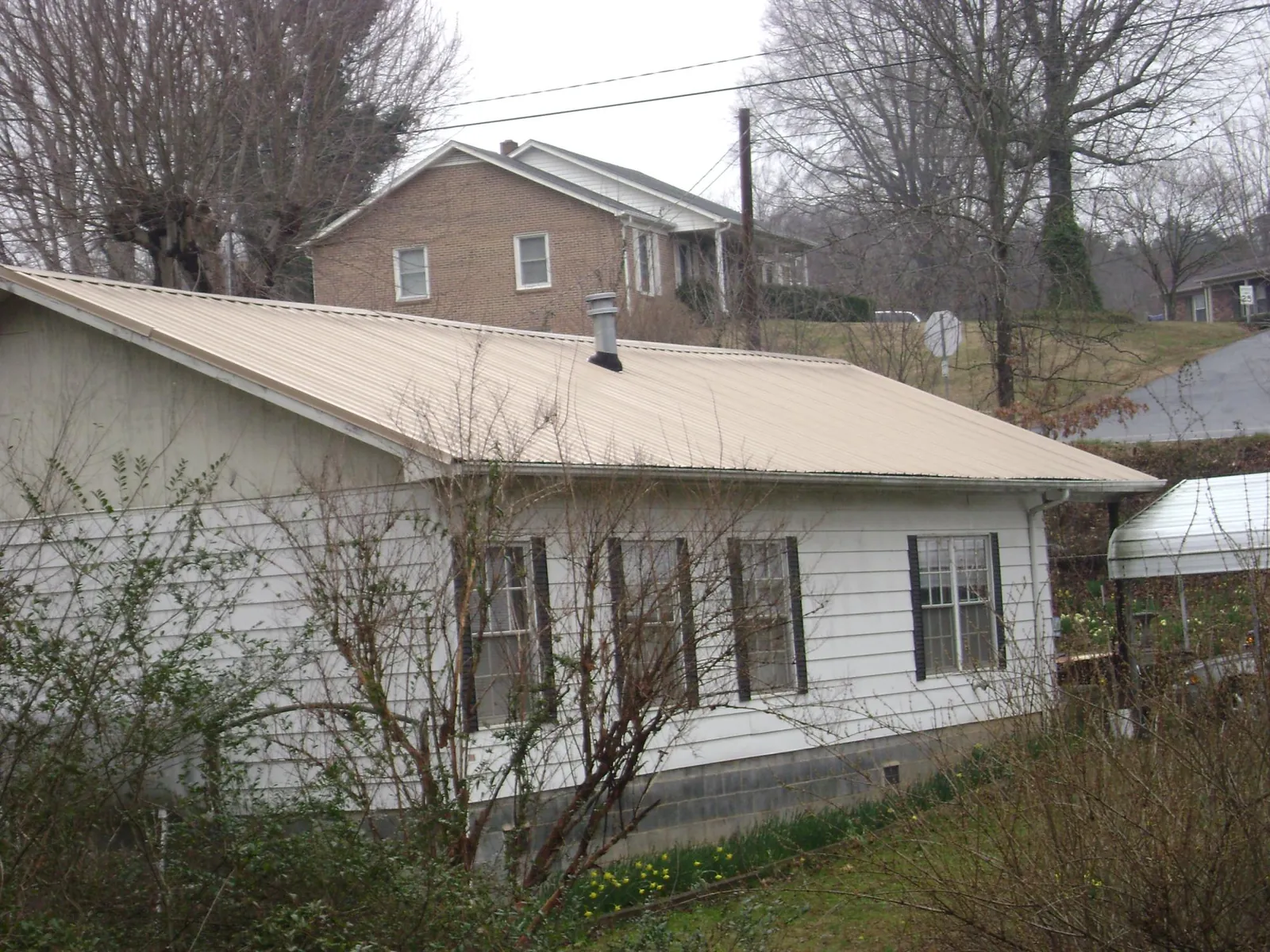 Tan metal roof on a white sided house set into a hillside — Commercial Roofing by Roofing Brothers in Beachwood